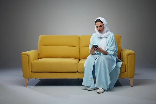 Saudi Woman on Yellow Sofa Using Smartphone in Studio