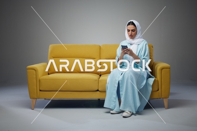 امرأة سعودية تستخدم الهاتف الذكي على أريكة في استوديو
