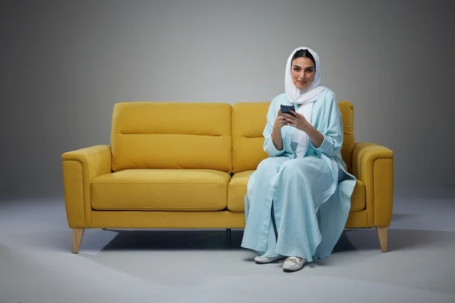 Saudi Arabian Woman Sitting on Yellow Sofa Using Smartphone