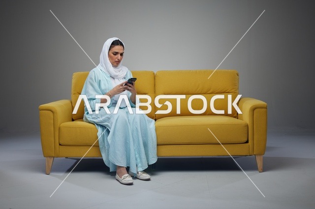 امرأة سعودية تستخدم الجوال على أريكة صفراء