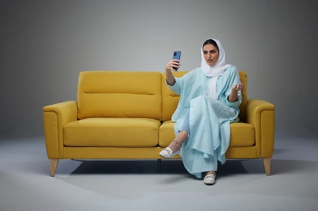 Saudi Woman on Yellow Sofa Taking Selfie with Phone