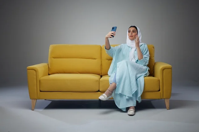 Saudi Woman Taking Selfie on Yellow Sofa in Studio Saudi Woman Taking Selfie on Yellow Sofa in Studio