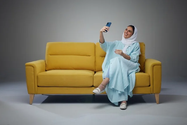 Saudi Woman Taking Selfie on Yellow Sofa Studio Portrait