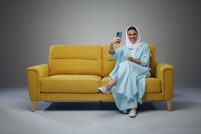 Saudi Woman on Yellow Sofa Taking Selfie with Phone
