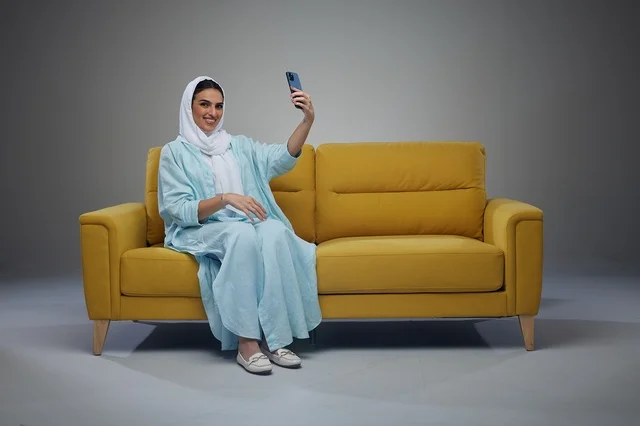 امرأة سعودية تلتقط صورة سيلفي على أريكة صفراء في الاستوديو