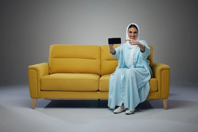 Saudi Woman on Yellow Sofa Pointing at Smartphone
