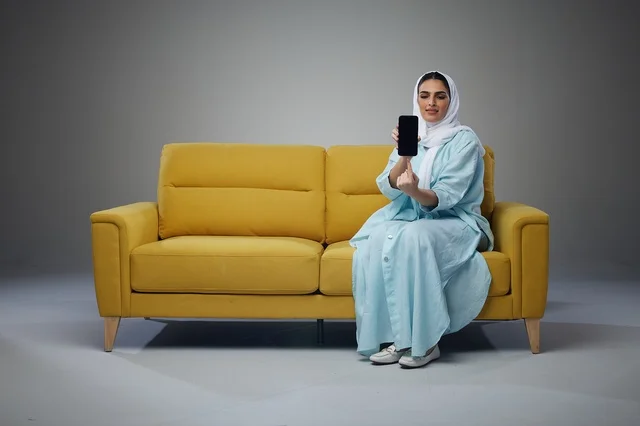 Saudi Woman on Yellow Sofa Holding Smartphone in Studio