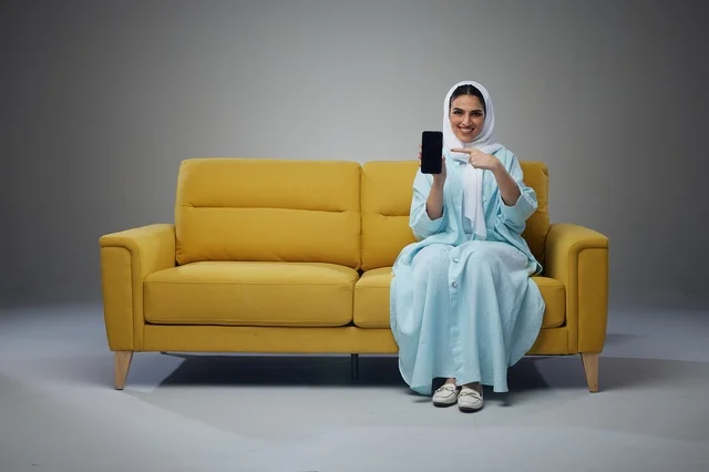 Saudi Woman Sitting on Yellow Sofa Holding Smartphone