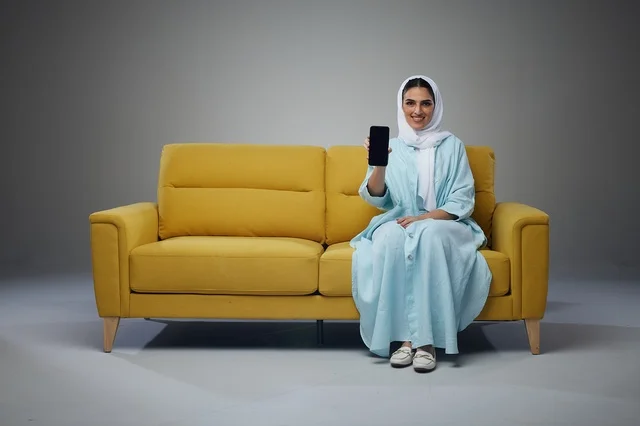 Saudi Woman on Yellow Sofa Holding Smartphone in Studio