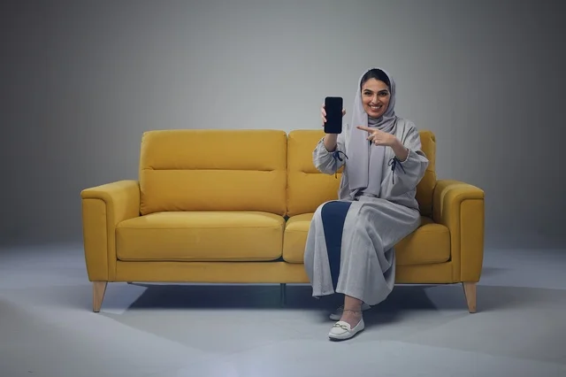 امرأة سعودية مع هاتف ذكي على أريكة صفراء