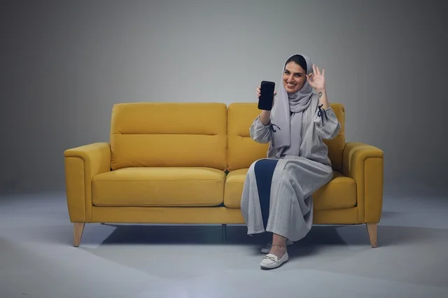 امرأة سعودية على أريكة صفراء تحمل هاتف ذكي