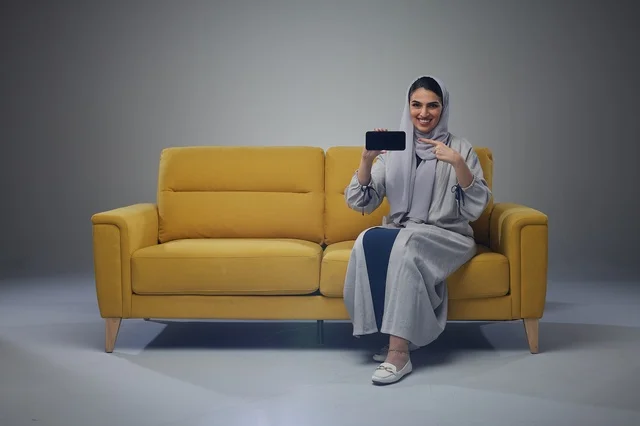 امرأة سعودية تحمل هاتف ذكي على أريكة صفراء