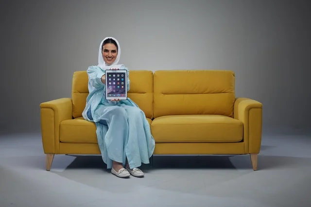 امرأة سعودية مع جهاز لوحي على أريكة صفراء