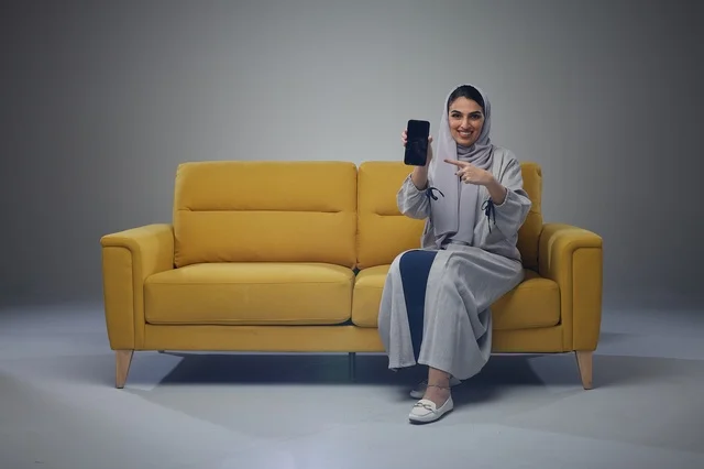 Saudi Woman Pointing at Smartphone on Yellow Sofa Studio Saudi Woman Pointing at Smartphone on Yellow Sofa Studio