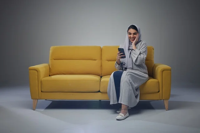 Saudi Woman on Yellow Sofa Using Smartphone in Studio