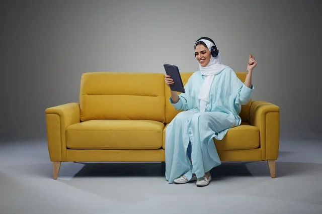 Saudi Woman on Yellow Sofa Using Tablet and Headphones