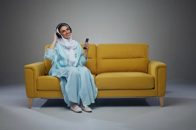 Saudi Woman with Headphones and Smartphone on Yellow Sofa