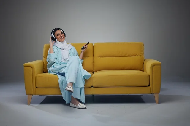 Saudi Woman on Yellow Sofa with Headphones and Phone