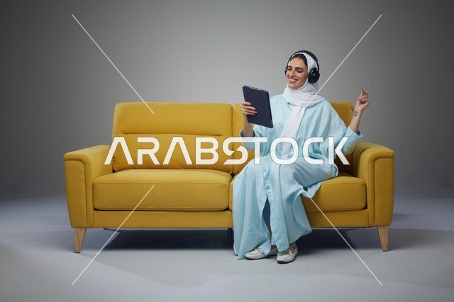 امرأة سعودية تستخدم جهاز لوحي وسماعات على أريكة