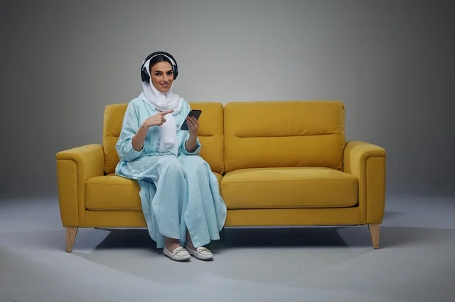 Saudi Woman on Yellow Sofa with Headphones and Phone