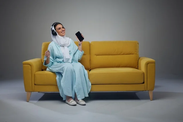 Saudi Woman on Yellow Sofa using Smartphone and Headphones