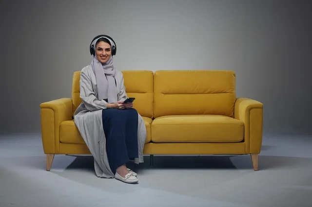 Saudi Woman on Yellow Sofa with Headphones and Smartphone