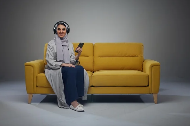 امرأة سعودية على أريكة صفراء مع هاتف وسماعات الرأس