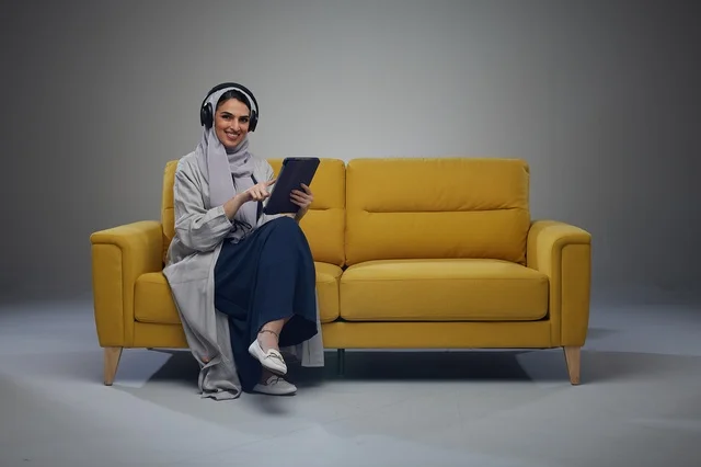 Saudi Woman Sitting on Sofa Using Tablet with Headphones