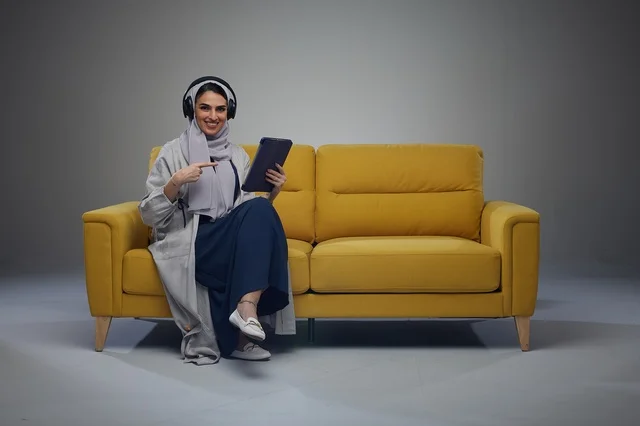 Saudi Woman on Yellow Sofa with Tablet and Headphones