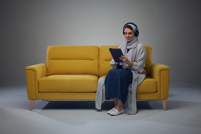Saudi Woman Sitting on Sofa Using Tablet with Headphones