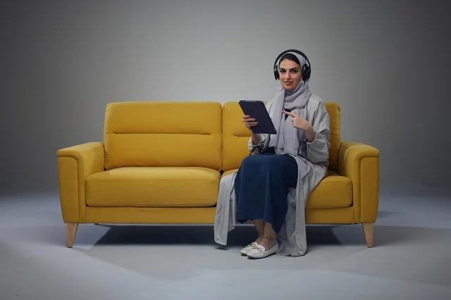 Saudi Woman with Tablet and Headphones on Yellow Sofa
