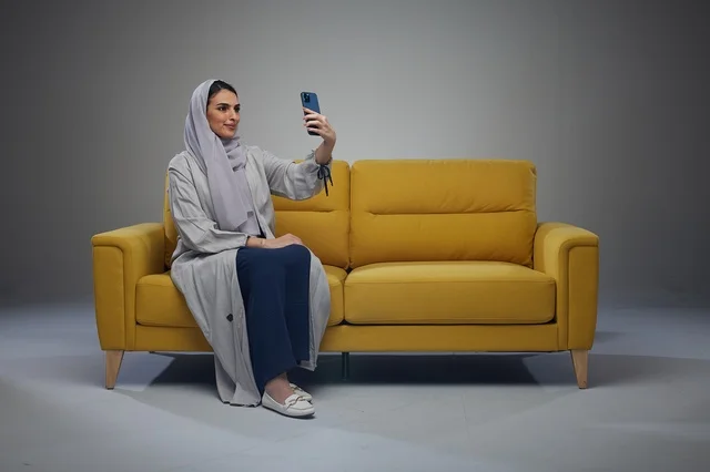 امرأة سعودية على أريكة صفراء تلتقط سيلفي بالهاتف الذكي