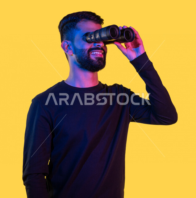 بورتريه لشاب عربي خليجي سعودي يمسك بيده ناظور و يشير بيده تجاه شئ ما رآه ، مشاهدة شيئا ما بإيماءات و تعابير وجه و يدين تدل على السعادة ، رؤية مستقبلية ، التخطيط المستقبلي ، أهداف و طموحات ، خلفية صفراء