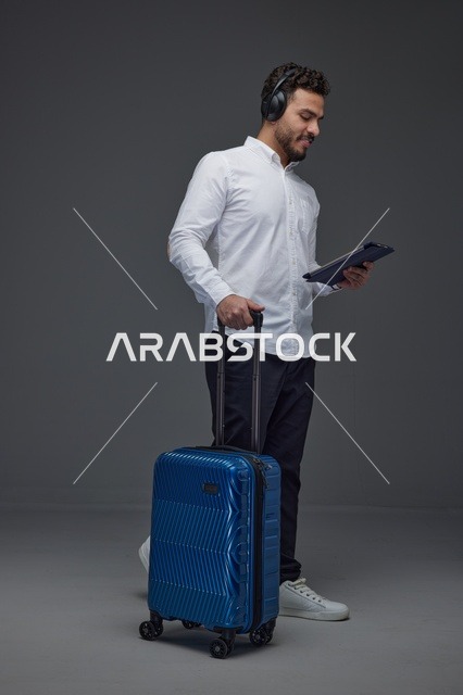 مسافر سعودي يستخدم جهاز لوحي مع حقيبة سفر زرقاء
