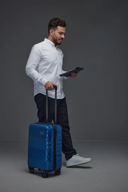 مسافر سعودي يستخدم جهازًا لوحيًا مع حقيبة سفر وسماعات