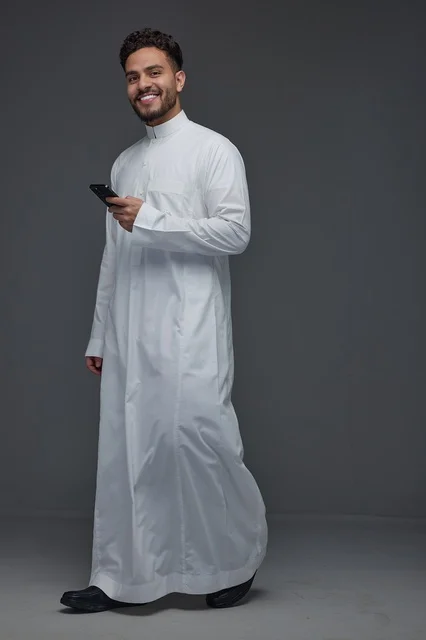 رجل سعودي يستخدم الهاتف الذكي مرتديًا الثوب التقليدي