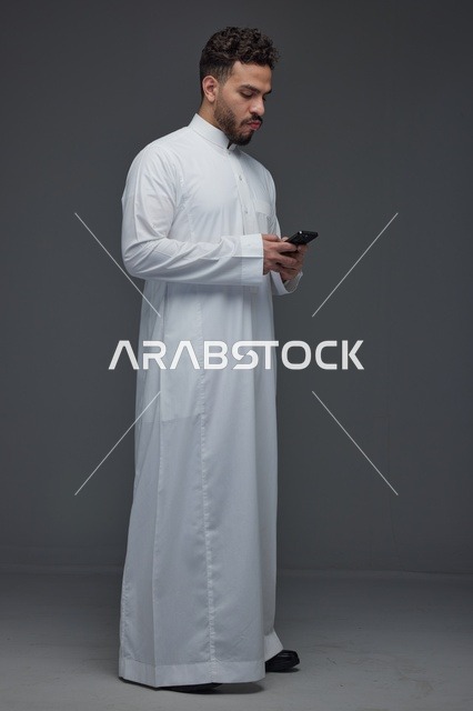 رجل سعودي يستخدم الهاتف الذكي مرتديًا الثوب التقليدي
