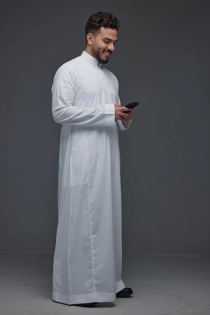 رجل سعودي يستخدم الهاتف الذكي مرتديًا الثوب التقليدي