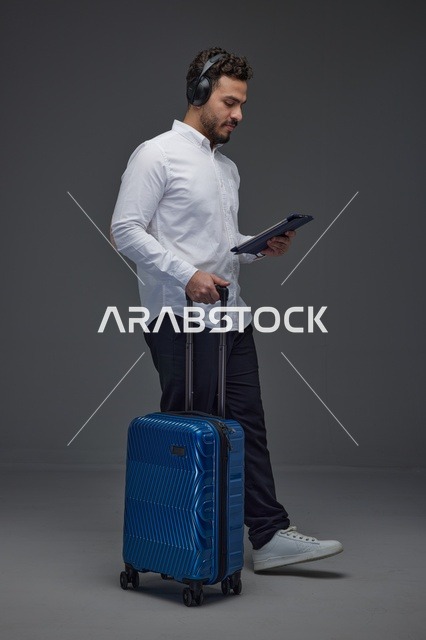 مسافر سعودي يستخدم جهازًا لوحيًا مع حقيبة سفر وسماعات