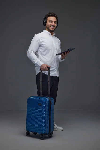 مسافر سعودي مع حقيبة سفر زرقاء وجهاز لوحي