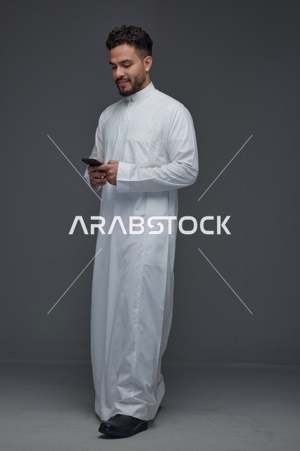 رجل سعودي بالثوب الأبيض يستخدم الهاتف الذكي