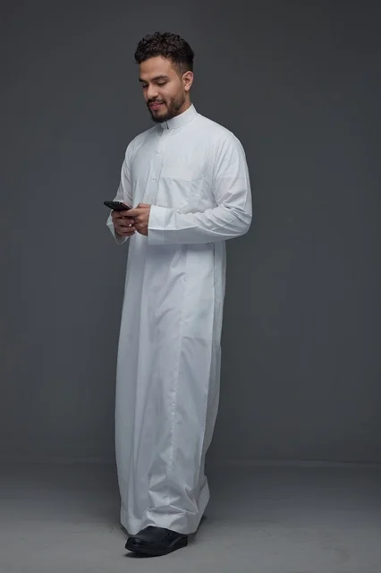 Saudi Man in White Thobe Using Smartphone