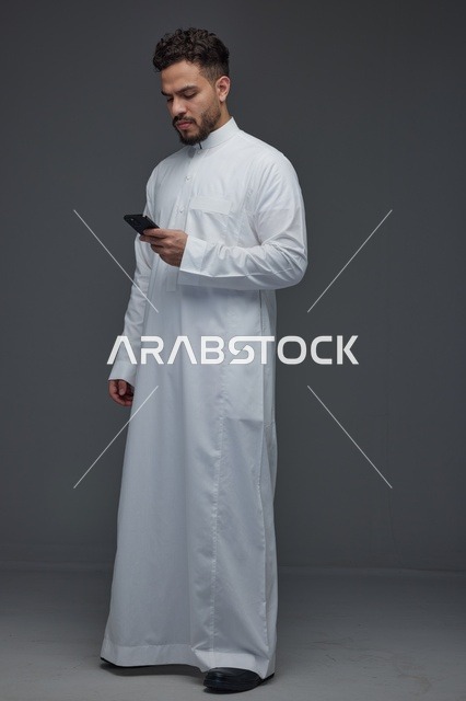 رجل سعودي بالثوب الأبيض يستخدم الهاتف الذكي في الاستوديو