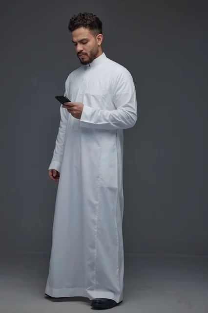 رجل سعودي بالثوب الأبيض يستخدم الهاتف الذكي في الاستوديو