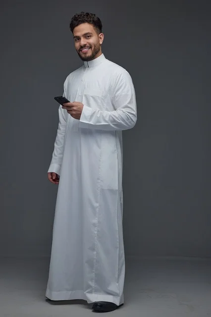 رجل سعودي يرتدي الثوب التقليدي ويحمل هاتفاً ذكياً