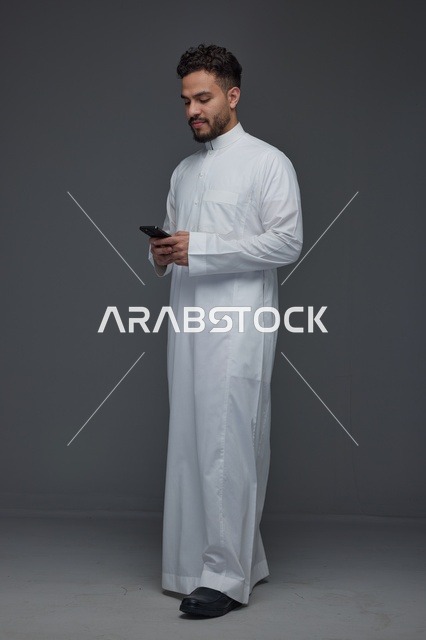 رجل سعودي بالثوب التقليدي يستخدم الهاتف الذكي