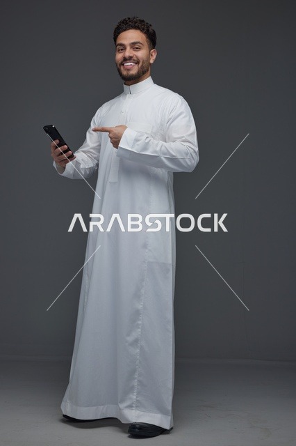 رجل سعودي بالثوب يشير إلى هاتف ذكي