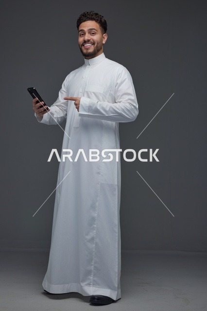 رجل سعودي بالثوب التقليدي يشير إلى هاتف ذكي