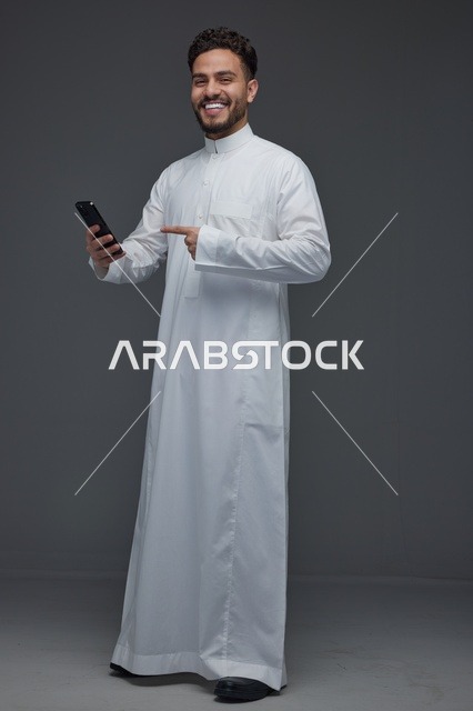 رجل سعودي يشير إلى هاتف ذكي بالثوب التقليدي