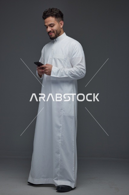 رجل سعودي بالثوب التقليدي يستخدم الهاتف في الاستوديو